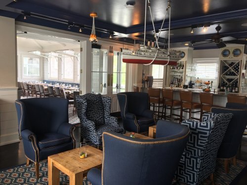 Cozy restaurant interior featuring blue patterned chairs, wooden tables, and a model ship hanging from the ceiling.