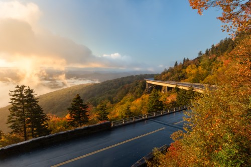 A scenic overlook with a winding road, surrounded by vibrant autumn foliage and misty mountains in the background.