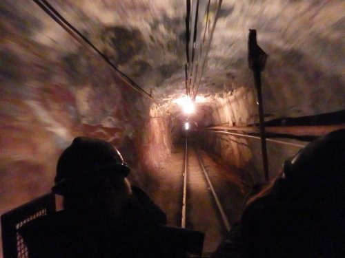 A dimly lit mine tunnel with tracks, viewed from a moving cart, creating a sense of depth and motion.