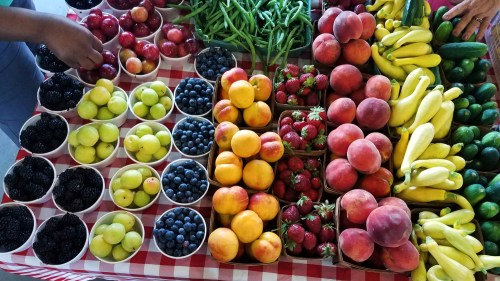 A colorful display of various fruits and vegetables in cups on a checkered tablecloth, including berries, peaches, and bananas.