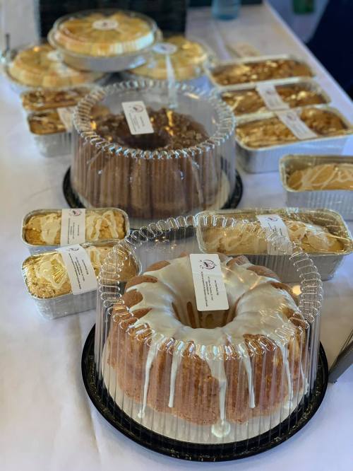 A table display of various cakes and desserts, including bundt cakes and baked goods in foil containers.
