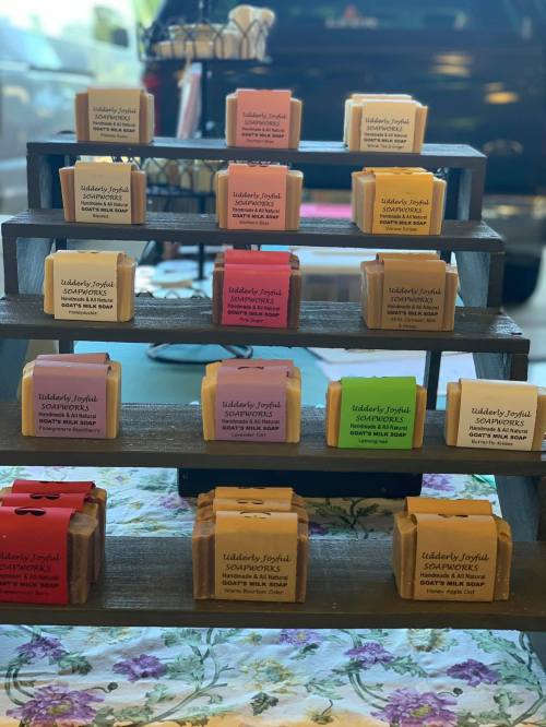A display of colorful soap bars arranged on a wooden stand, labeled with various scents and names.