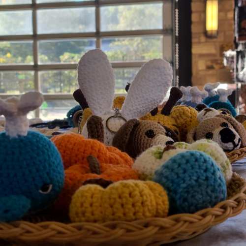 A collection of colorful crocheted animals and pumpkins displayed in a woven basket, with sunlight streaming in.
