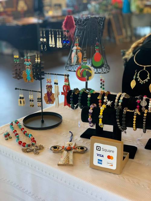 A display of colorful handmade jewelry, including earrings, necklaces, and bracelets, with a payment sign.