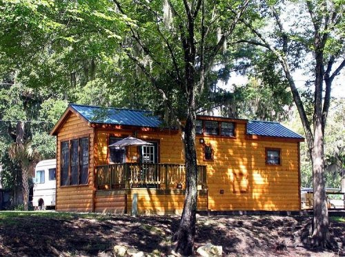 A cozy wooden cabin with a blue metal roof, surrounded by trees and greenery.