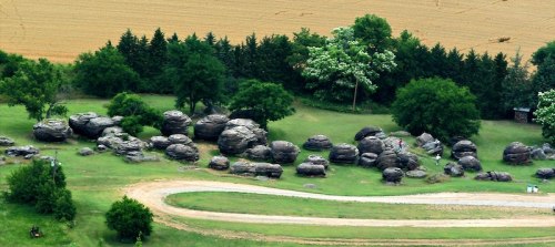 Aerial view of large boulders scattered across a grassy area, surrounded by trees and a winding dirt path.