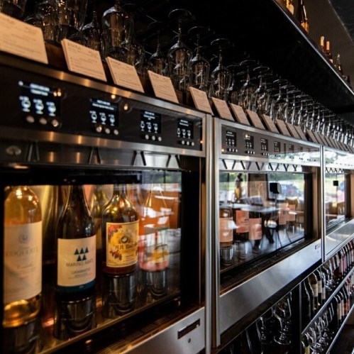 A row of wine dispensers showcasing various bottles and glasses in a modern bar setting.