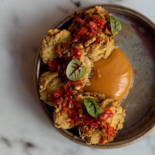A plate of crispy fried food topped with a vibrant salsa and a dollop of creamy sauce, garnished with small leaves.