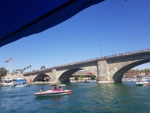 A view of a stone bridge over water, with boats and palm trees under a clear blue sky.