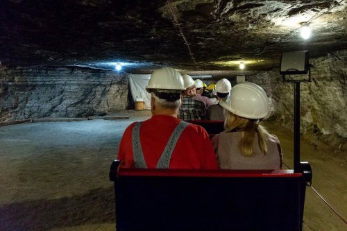 A group of people wearing hard hats sits in a mine cart inside a dimly lit underground mine.