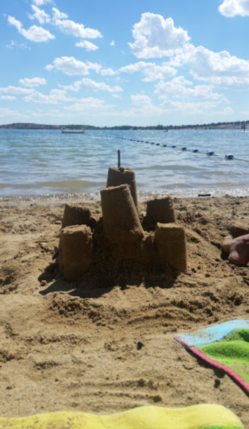 A sandcastle on a beach with water in the background and a blue sky dotted with clouds.