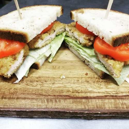 A sandwich with crispy chicken, lettuce, and tomato, served on two slices of white bread on a wooden cutting board.