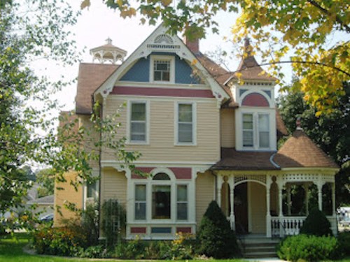 A charming Victorian-style house with colorful siding, intricate details, and a welcoming porch surrounded by greenery.