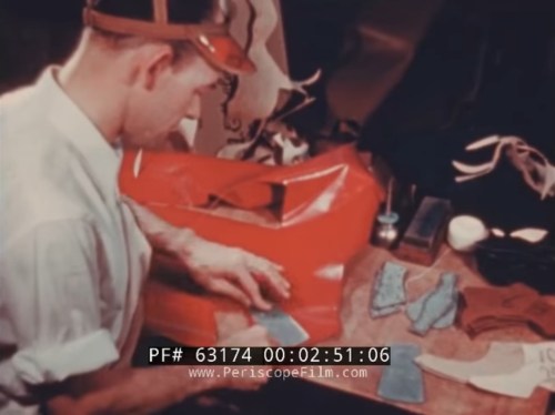 A man works at a table, cutting blue fabric pieces for a project, with various tools and materials around him.