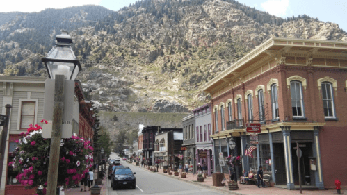 A scenic street view with historic buildings, flowers, and a mountain backdrop in a small town.