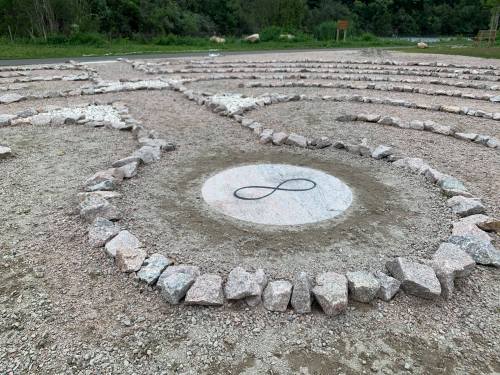 A stone labyrinth with an infinity symbol at its center, surrounded by a natural landscape.