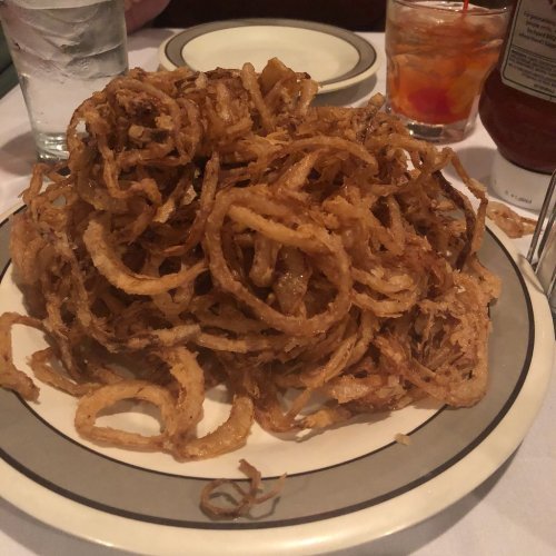 A large plate piled high with crispy, golden-brown onion rings, served in a casual dining setting.