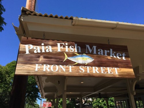 Sign for Paia Fish Market on Front Street, featuring a fish graphic against a wooden background. Clear blue sky above.