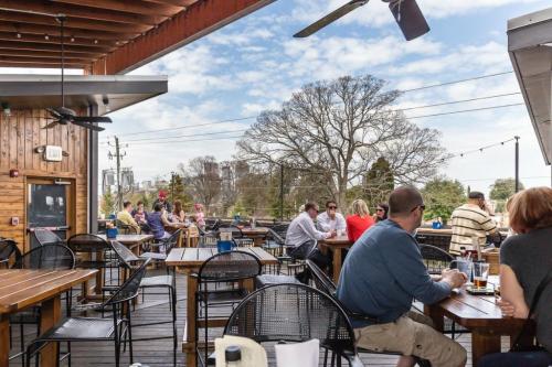 Outdoor dining area with wooden tables, people socializing, and a clear blue sky in the background.