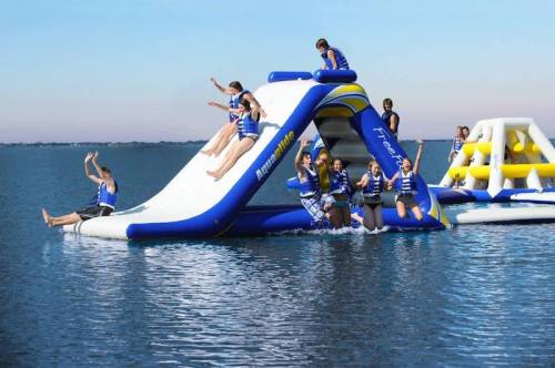 A group of people enjoying an inflatable water slide and obstacle course on a lake, wearing life jackets.