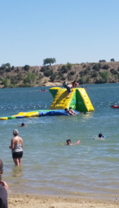 A colorful inflatable water slide on a lake, with people swimming and playing nearby on a sunny day.