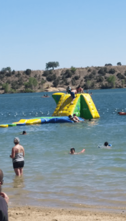 A colorful inflatable water slide on a lake, with people swimming and playing nearby on a sunny day.