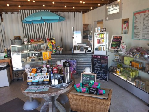 A cozy shop interior featuring a counter, snacks, drinks, and colorful decor under a blue umbrella.