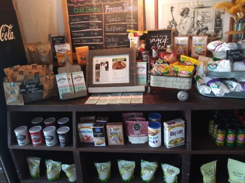 A wooden shelf displays various food items, including snacks, mixes, and drinks, with a menu and recipe in the center.