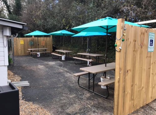 Outdoor seating area with wooden tables and turquoise umbrellas, enclosed by wooden fences.