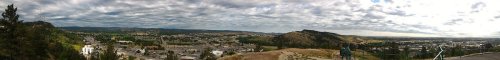 Panoramic view of a valley with rolling hills, a town below, and a cloudy sky above.