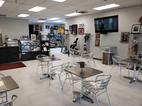 A modern café interior with metal tables, a display case, and a TV showing a movie in a well-lit space.