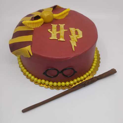 A round cake decorated in red and gold, featuring "HP," glasses, a lightning bolt, and a wand.