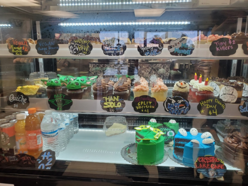 Display case filled with colorful cupcakes and desserts, labeled with fun names and flavors.