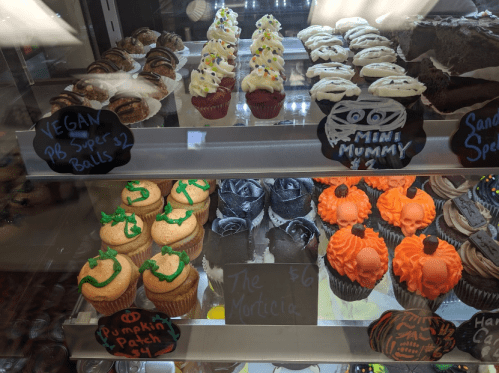 A display of colorful cupcakes and treats, including vegan options and Halloween-themed designs.