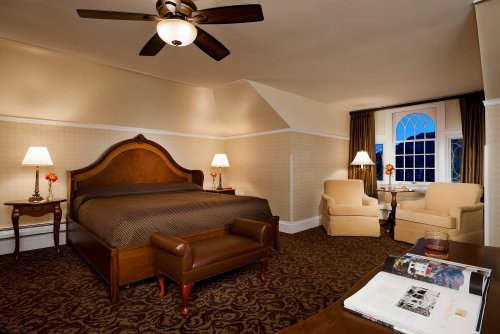 Cozy hotel room with a large bed, two armchairs, a window, and warm lighting, featuring elegant decor and a plush carpet.
