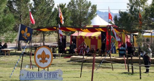 A colorful tent with flags and a sign reading "Adrian Empire," set in a grassy area with people and hay bales.