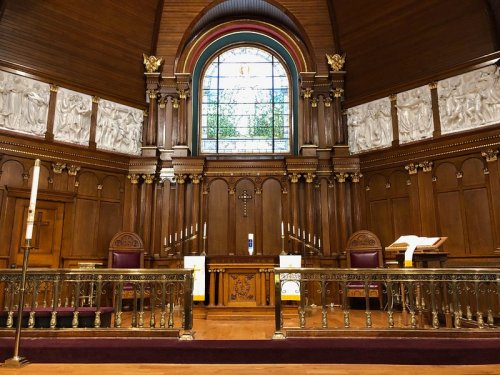 Interior of a wooden church altar with a stained glass window, candles, and ornate carvings on the walls.