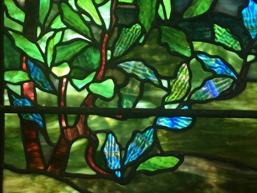 Stained glass featuring vibrant green leaves and branches, with hints of blue and red accents.