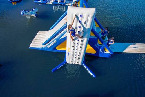 A child climbs an inflatable water slide with others playing on nearby inflatable structures in a lake.