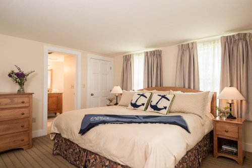 Cozy bedroom with a large bed, decorative pillows, wooden furniture, and soft lighting from windows.