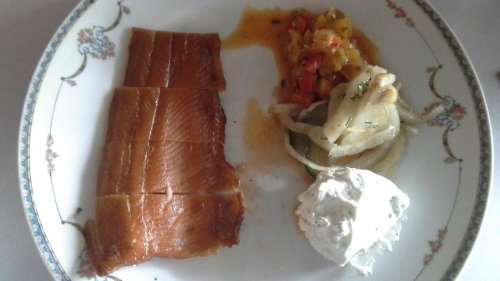 A plate with sliced smoked fish, a vegetable medley, and a dollop of creamy sauce, all on a decorative dish.