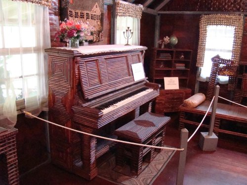 A unique piano made of woven materials, displayed in a cozy room with floral decor and wooden furniture.
