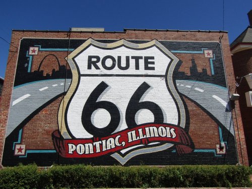 Mural of Route 66 in Pontiac, Illinois, featuring a highway sign and city skyline on a brick wall.