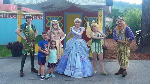 A group of children and costumed characters pose together in a colorful outdoor setting.