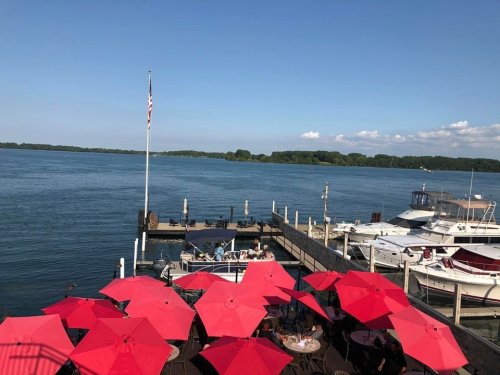 A scenic view of a waterfront with red umbrellas, boats docked, and a clear blue sky.