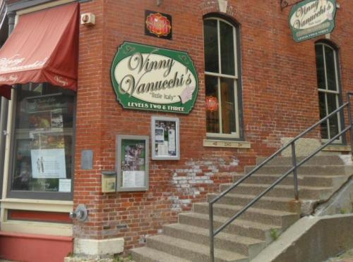 Exterior of Vinny Vanucci's restaurant, featuring a brick facade, green signage, and stairs leading to the entrance.