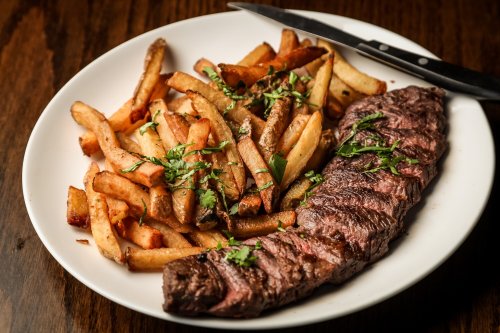 A plate of grilled steak garnished with herbs, served alongside crispy French fries.