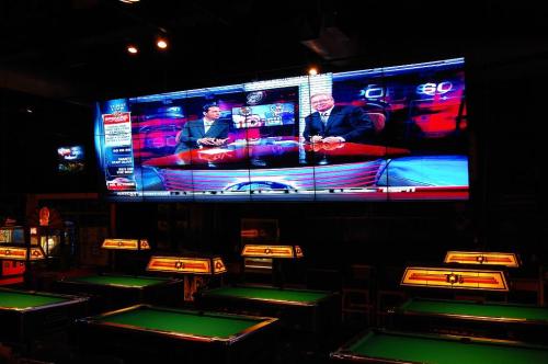 A large TV screen displays two hosts discussing sports, with pool tables visible in the foreground.