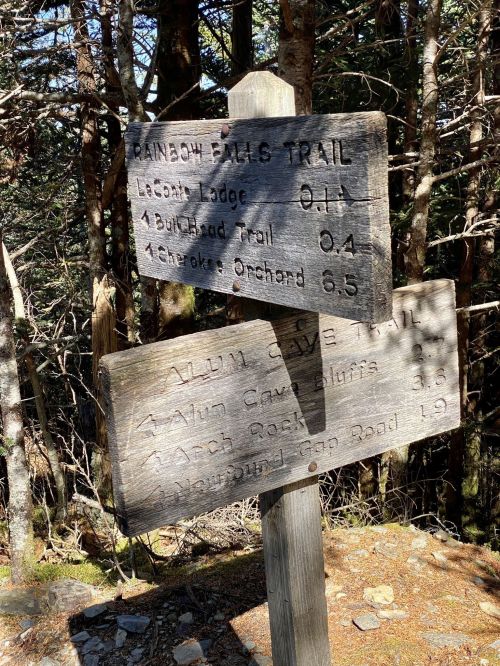 Wooden trail signs indicating distances to various locations, surrounded by trees.