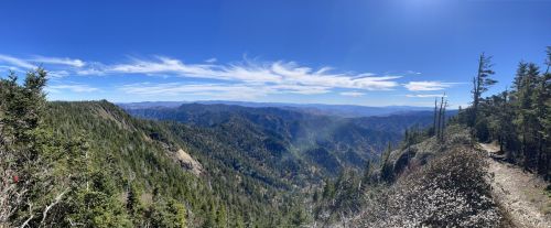 Panoramic view of a mountainous landscape with lush greenery and a clear blue sky dotted with wispy clouds.